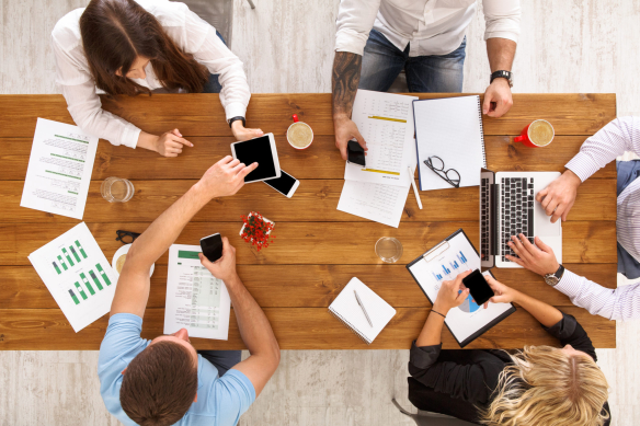 Group of busy business people working in office, top view of wooden table with mobile phones, laptop, tablet and documents papers with diagram. Men and women team together have brainstorm discussion.